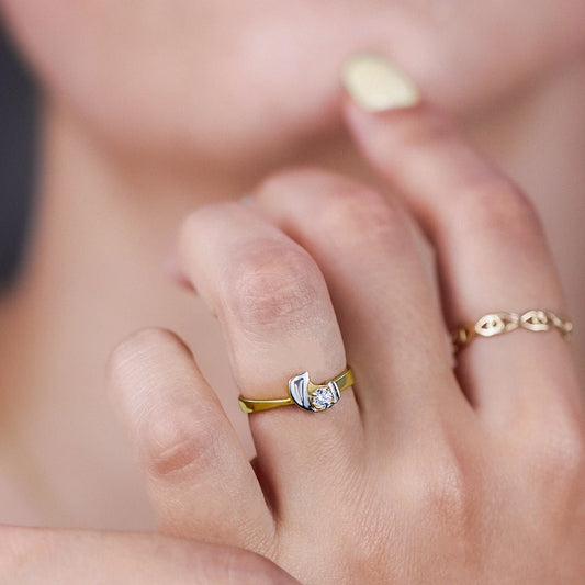 Mano de mujer usando un anillo del aro en oro amarillo con forma de onda en el centro en oro blanco de 18 quilates y cristal redondo en el centro de color blanco de Joyería Caracas.
