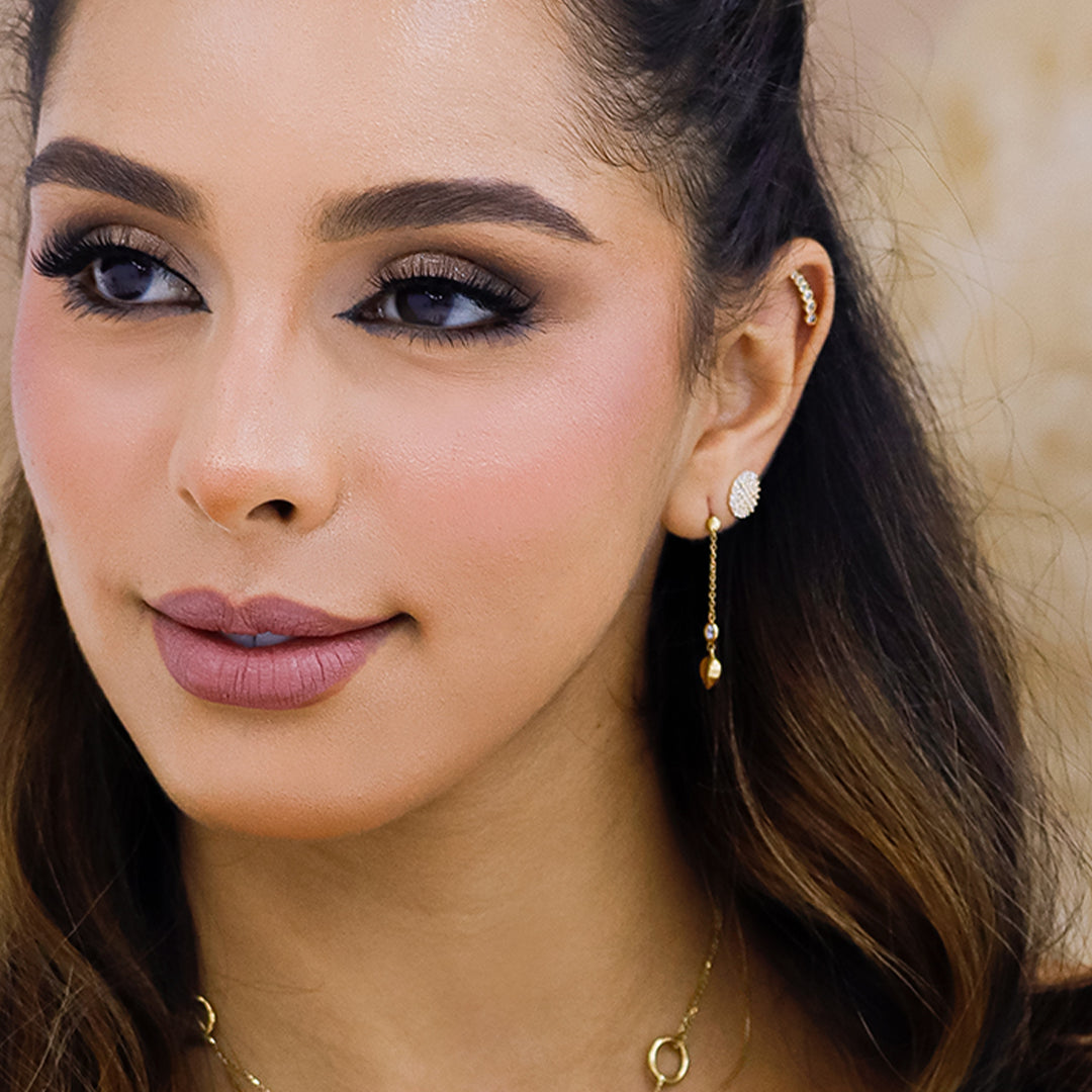 Oreja de mujer con arete largo con forma de corazón en la punta en oro amarillo de 18 quilates y cristal de color blanco.