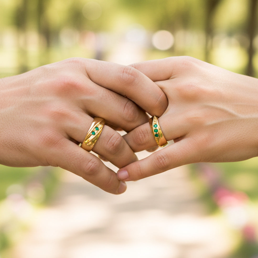 Manos de una pareja usando unas argollas de matrimonio en oro amarillo con cristales verdes de Joyería Caracas. 