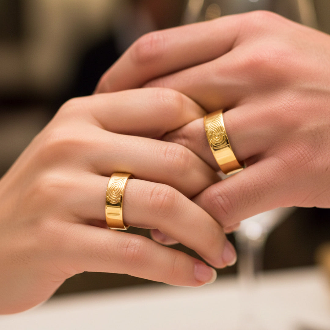 Manos de una pareja usando unas argollas en oro amarillo grabadas con huellas dactilares de 18 quilates de Joyería Caracas.