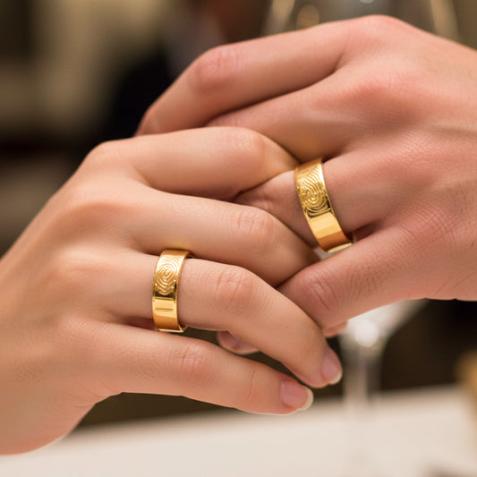 Manos de una pareja usando unas argollas en oro amarillo grabadas con huellas dactilares de 18 quilates de Joyería Caracas.