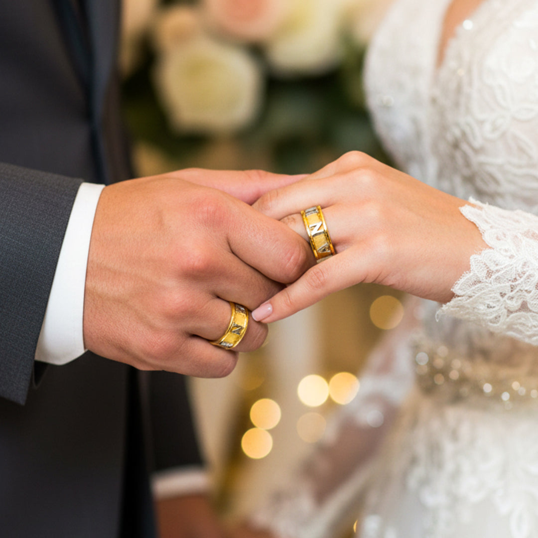Manos de una pareja usando unas argollas de matrimonio personalizadas con el nombre en oro amarillo y blanco de 18 quilates de Joyería Caracas. 