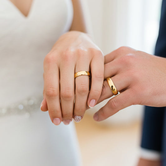 Manos de una pareja usando unas argollas de matrimonio en oro amarillo planas de 18 quilates de Joyería Caracas. 