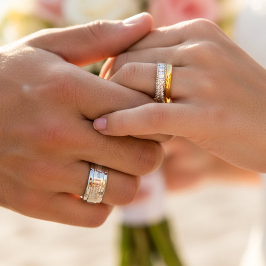 Manos de una pareja usando unas argollas de matrimonio en oro blanco y amarillo de 18 quilates con cristales de Joyería Caracas. 
