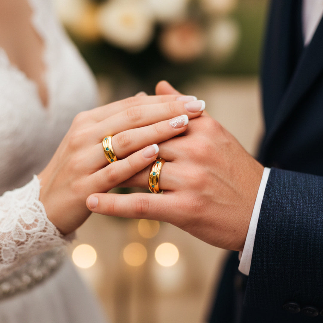 Manos de una pareja usando unas argollas de matrimonio en oro amarillo de 18 quilates con 3 cristales verdes de Joyería Caracas. 