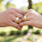 Manos de una pareja usando unas argollas de matrimonio en oro amarillo de 18 quilates con cristales verdes y blancos de Joyería Caracas. 