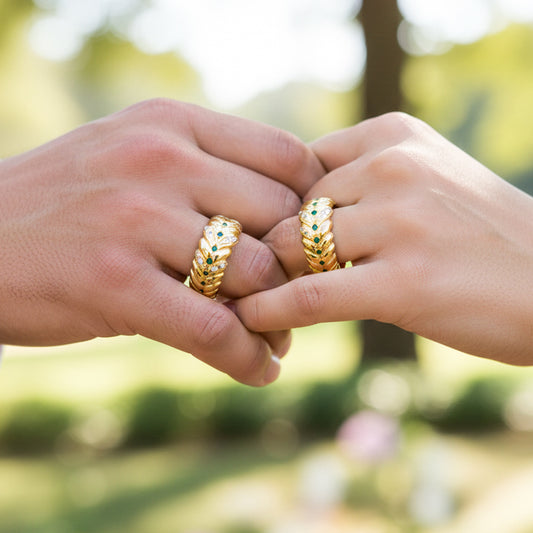 Manos de una pareja usando unas argollas de matrimonio en oro amarillo de 18 quilates con cristales verdes y blancos de Joyería Caracas. 
