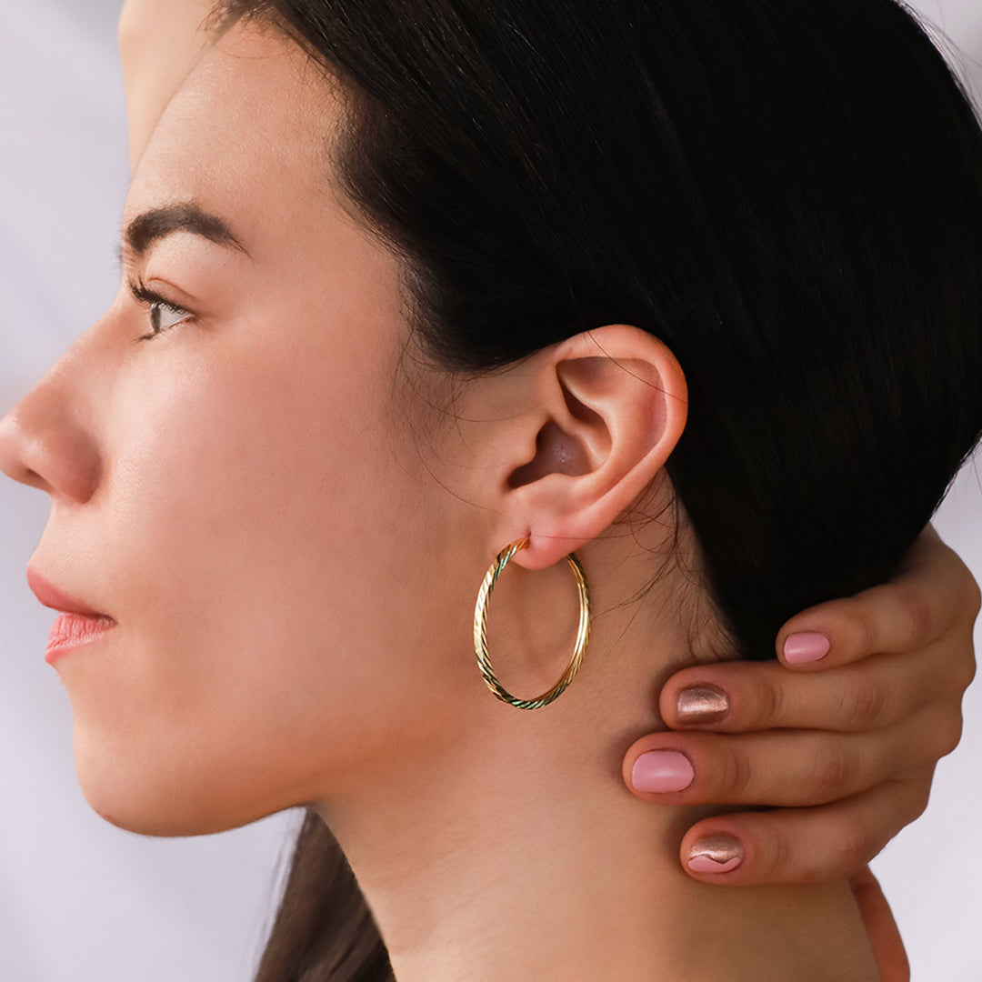 Oreja de mujer usando candongas square en forma de tubo con textura diamantada en oro amarillo de 18 quilates de Joyería Caracas.