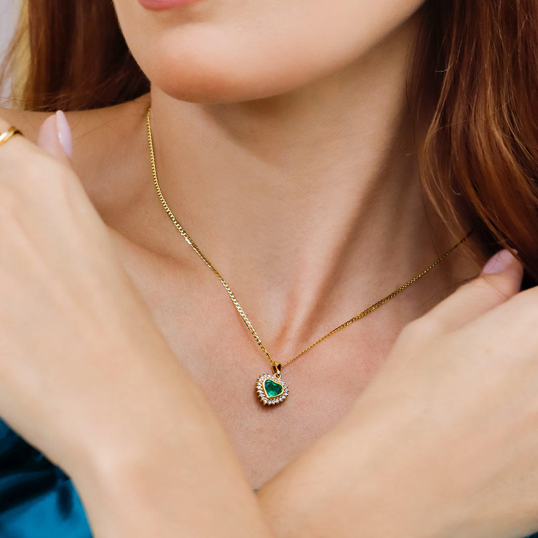 Cuello de mujer con cadena y dije en forma de corazón en oro amarillo de 18 quilates, esmeralda en forma de corazón y diamantes alrededor de color blanco, hecho en Joyería Caracas. 