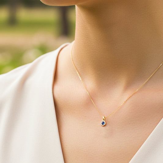 Cuello de modelo usando una cadena con un dije en forma redonda en oro amarillo de 18 quilates con cristal azul y blancos de Joyería Caracas.