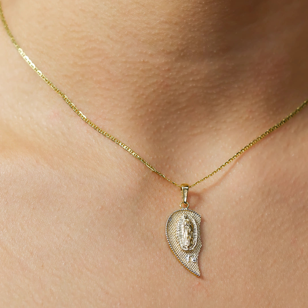 Cuello de mujer usando un dije de medio corazón de la Virgen de Guadalupe en oro amarillo de 18 quilates de Joyería Caracas. 