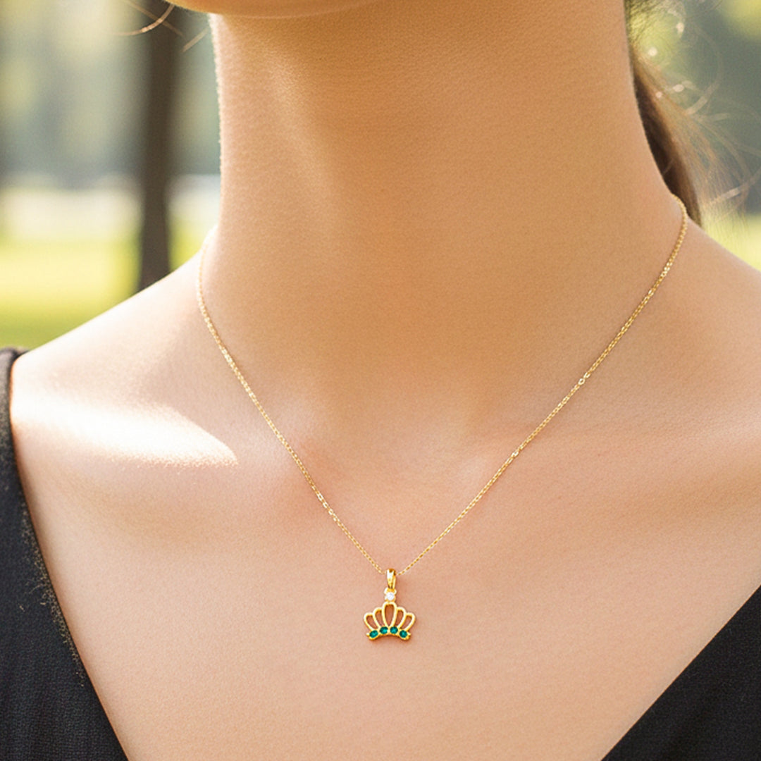 Cuello de modelo usando una cadena con un dije en forma de corona en oro amarillo de 18 quilates con cristales verdes de Joyería Caracas.