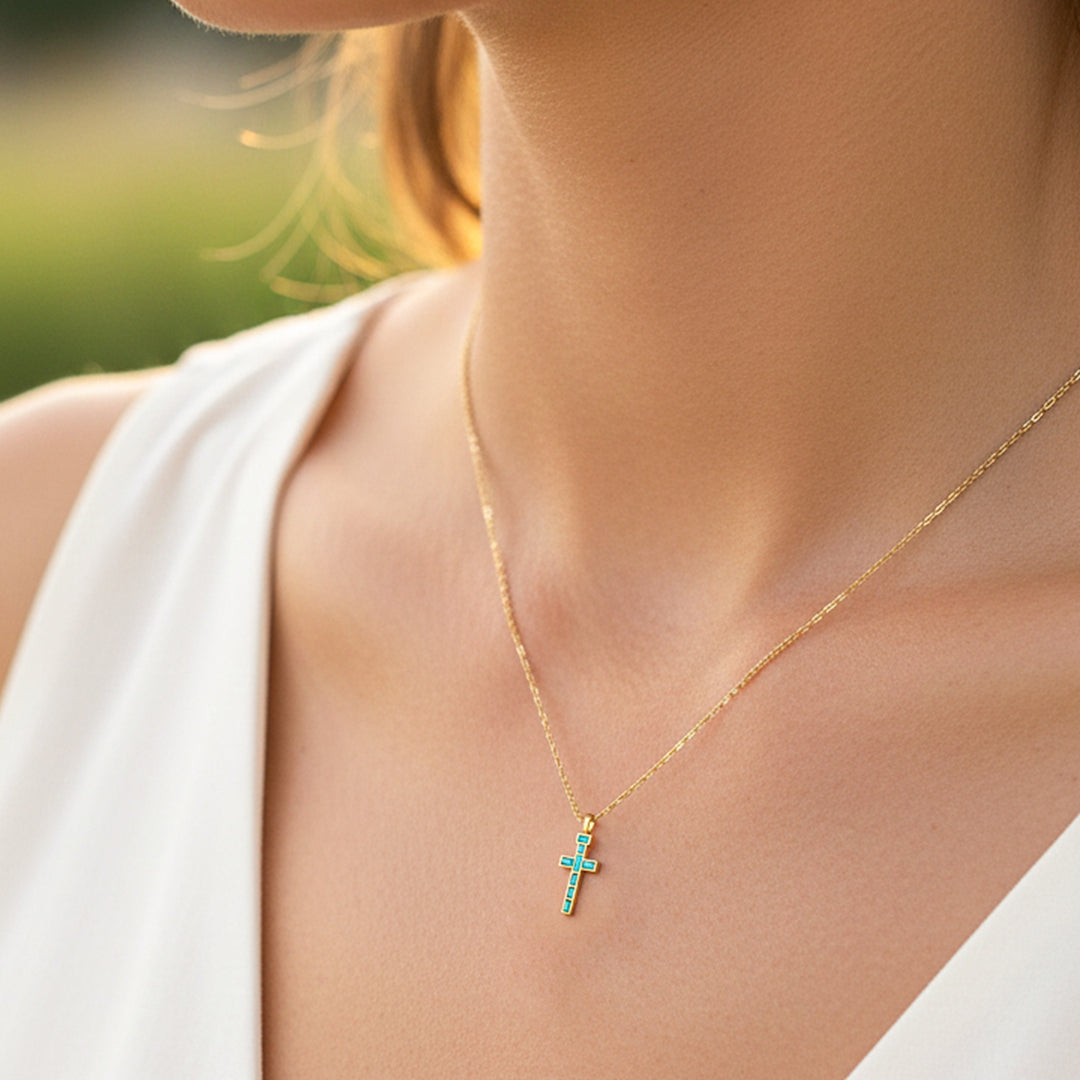 Cuello de modelo usando una cadena con un dije en forma de cruz oro amarillo de 18 quilates con Esmeraldas de Joyería Caracas.