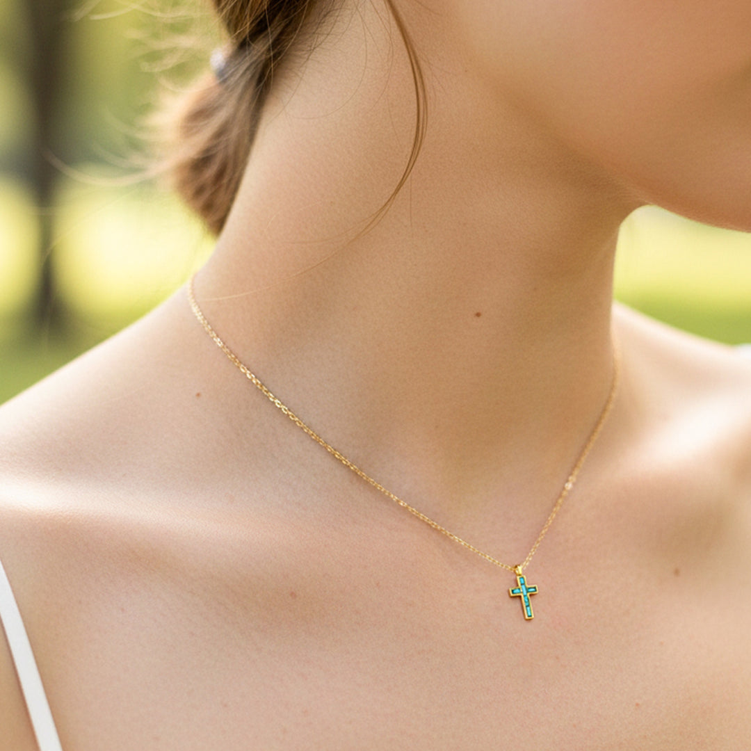 Cuello de modelo usando una cadena con un dije en forma de cruz oro amarillo de 18 quilates con Esmeraldas de Joyería Caracas.