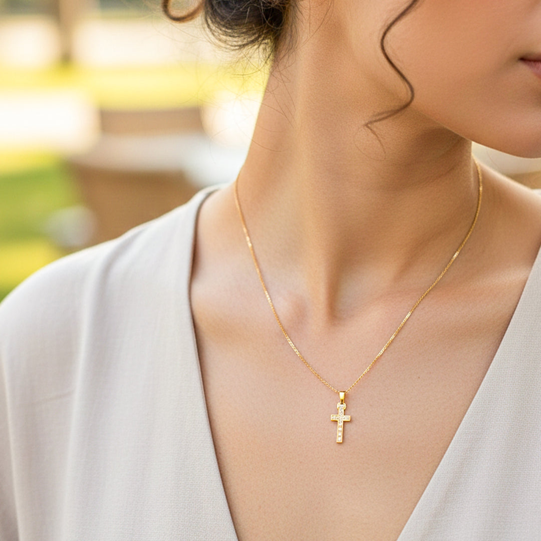 Cuello de modelo usando una cadena con un dije en forma de cruz en oro amarillo de 18 quilates con cristales de Joyería Caracas.