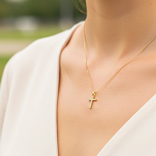 Cuello de modelo usando una cadena con un dije en forma de cruz en oro amarillo de 18 quilates con cristales de Joyería Caracas.