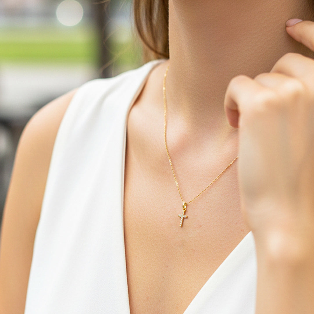 Cuello de modelo usando una cadena con un dije en forma de cruz en oro amarillo de 18 quilates con cristales de Joyería Caracas.