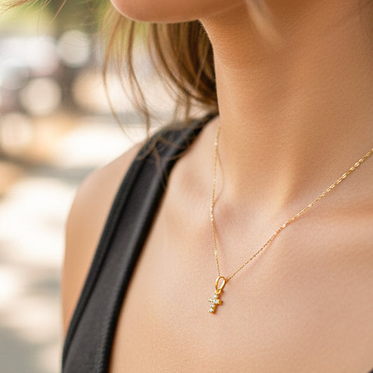 Cuello de modelo usando una cadena con un dije en forma de cruz en oro amarillo de 18 quilates con cristales de Joyería Caracas.