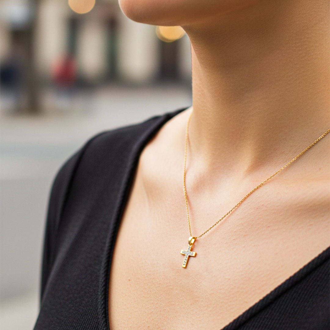 Cuello de modelo usando una cadena con un dije en forma de cruz en oro amarillo de 18 quilates con cristales de Joyería Caracas.