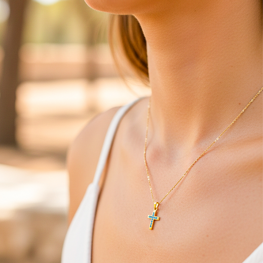 Cuello de modelo usando una cadena con un dije en forma de cruz en oro amarillo de 18 quilates con cristales azules de Joyería Caracas.