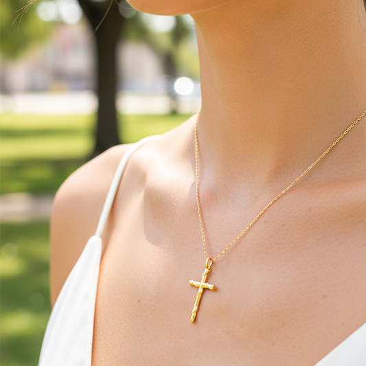 Cuello de modelo usando una cadena con un dije en forma de cruz entorchada en oro amarillo de 18 quilates de Joyería Caracas.