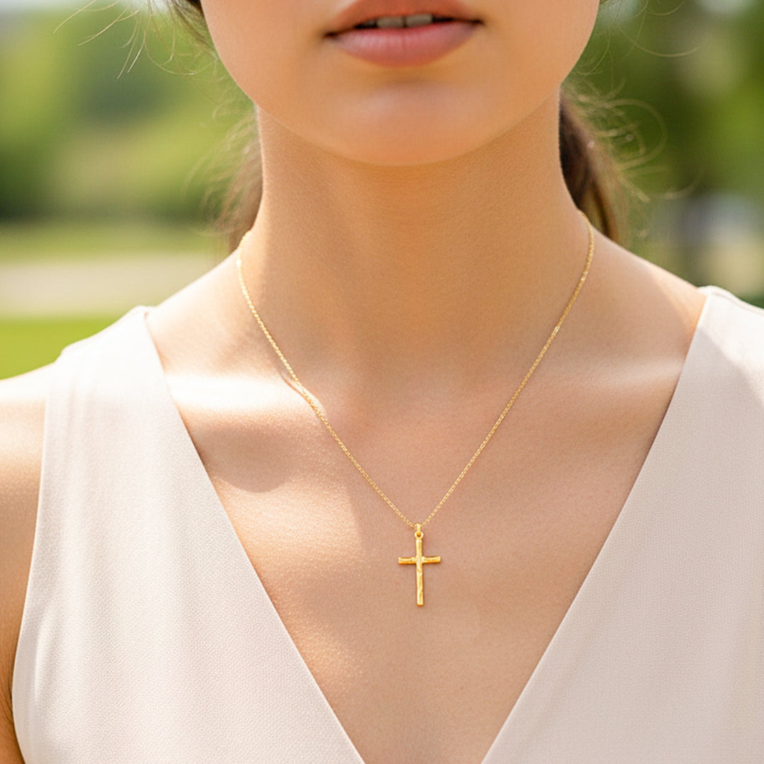 Cuello de modelo usando una cadena con un dije en forma de cruz con textura de tronco en oro amarillo de 18 quilates de Joyería Caracas.