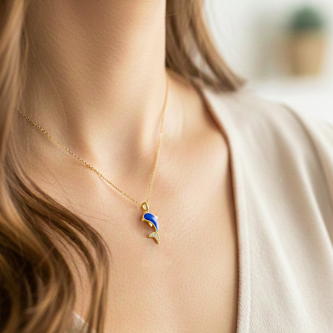 Cuello de modelo usando una cadena con un dije en forma de delfín en oro amarillo de 18 quilates con fondo en azul y cristales blancos de Joyería Caracas.