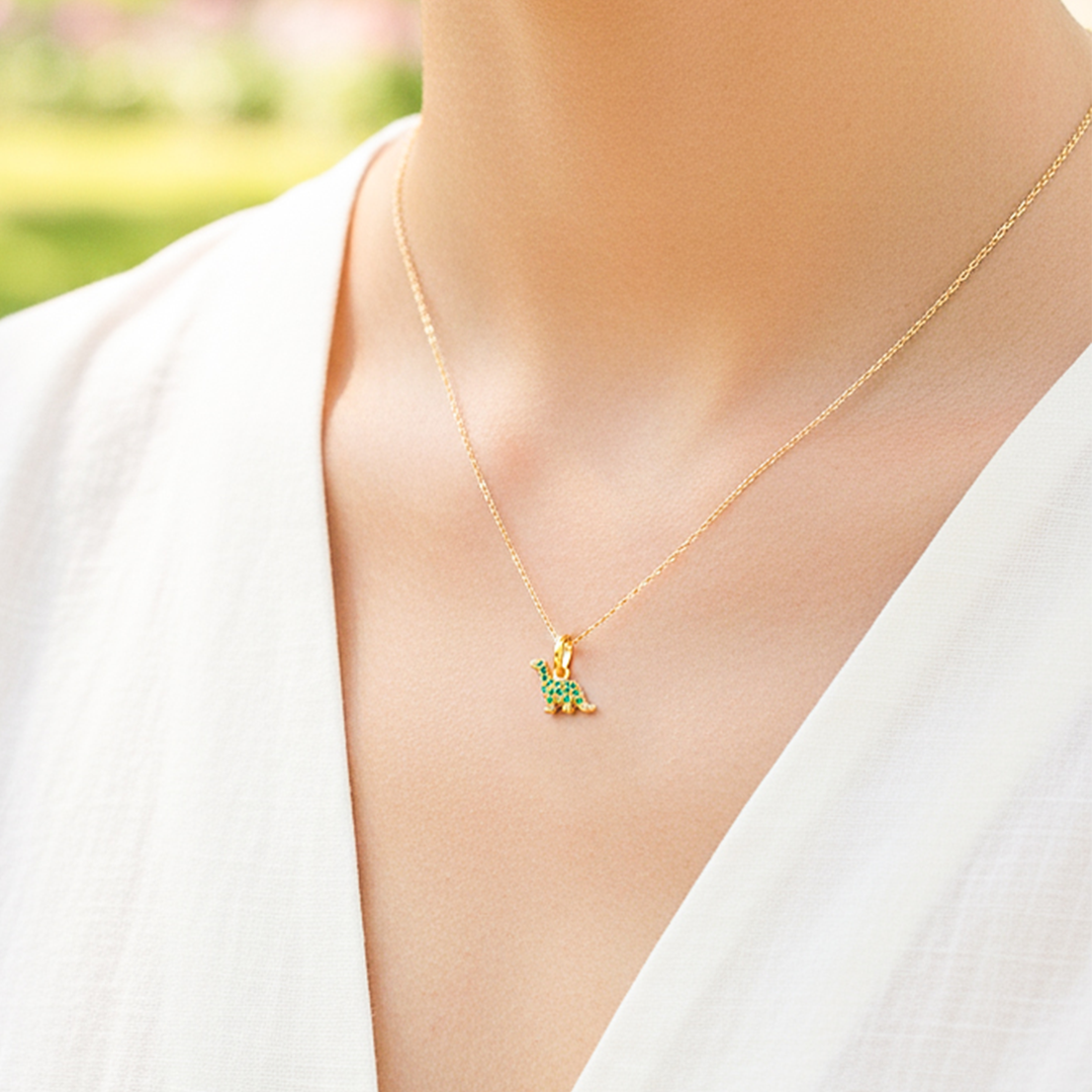 Cuello de modelo usando una cadena con un dije en forma de Dinosaurio en oro amarillo de 18 quilates con cristales de color verde de Joyería Caracas.