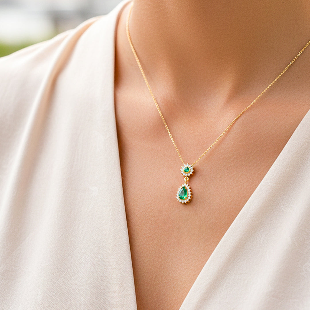 Cuello de modelo usando una cadena con un dije en oro amarillo de 18 quilates con Esmeraldas en forma de gota de Joyería Caracas.