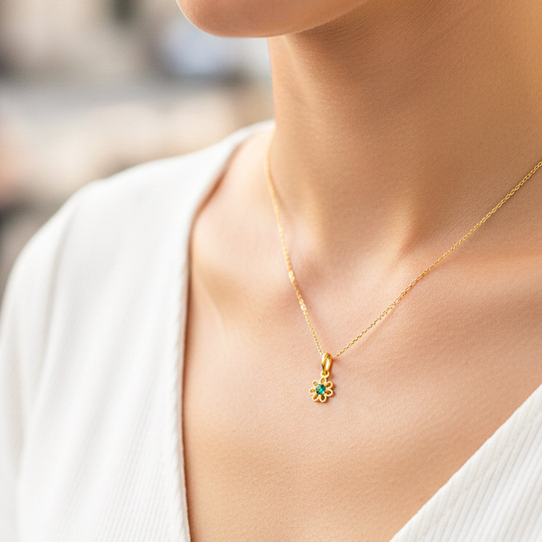 Cuello de modelo usando una cadena con un dije en forma de flor con pétalos en oro amarillo de 18 quilates con cristal verde de Joyería Caracas.
