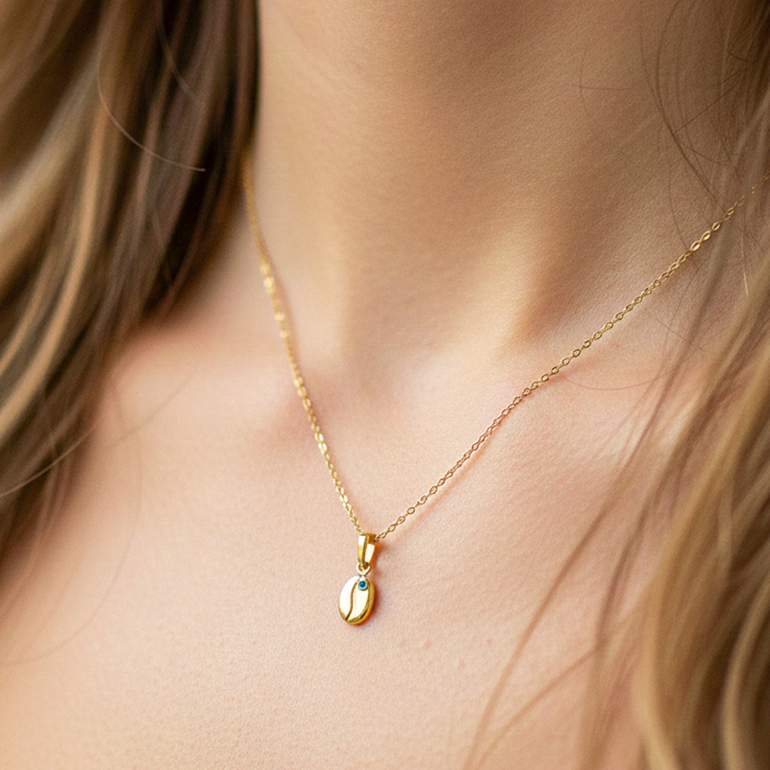 Cuello de modelo usando una cadena con un dije en forma de grano de café en oro amarillo de 18 quilates con Esmeralda de Joyería Caracas.