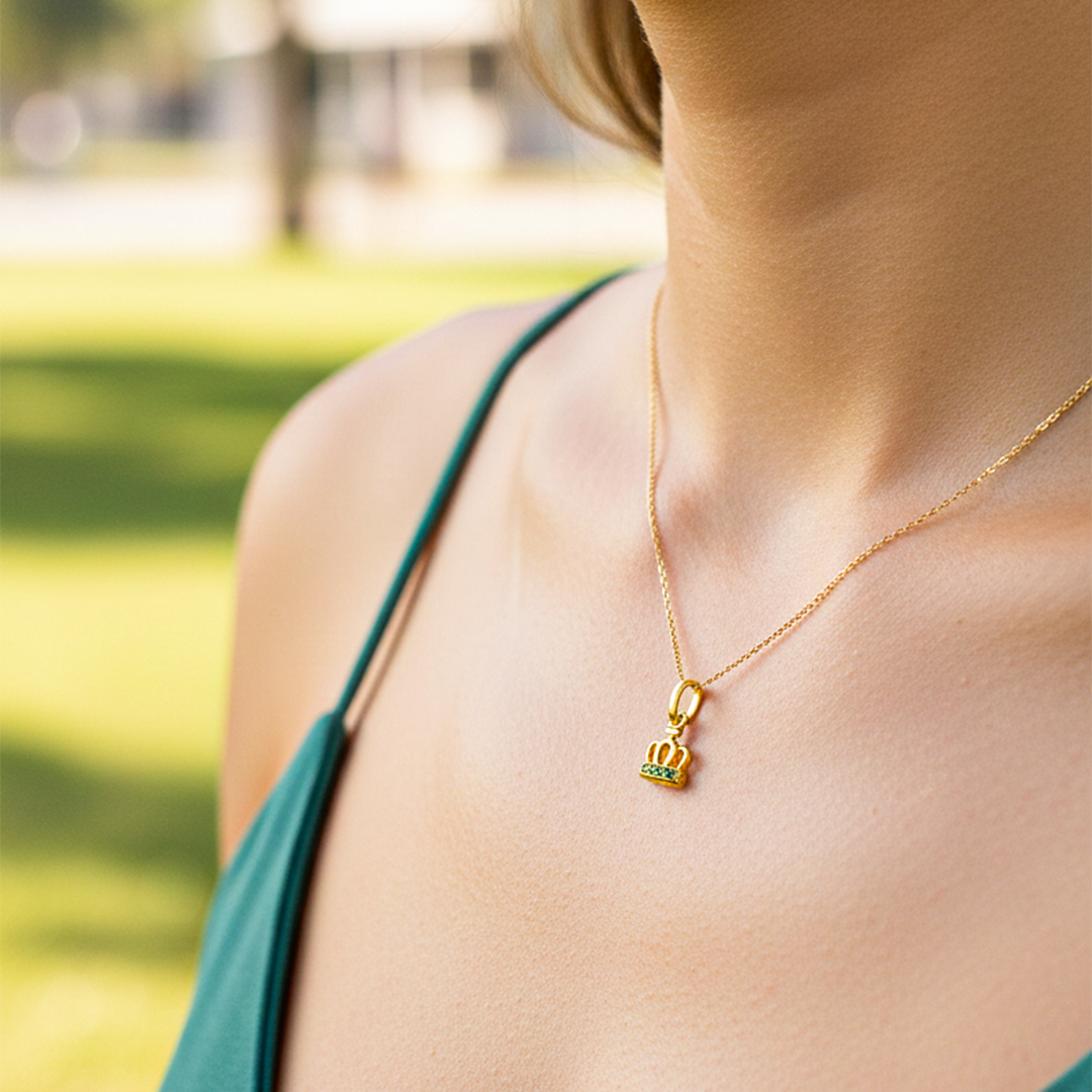 Cuello de modelo usando una cadena con un dije en forma de corona en oro amarillo de 18 quilates con cristales verdes de Joyería Caracas.