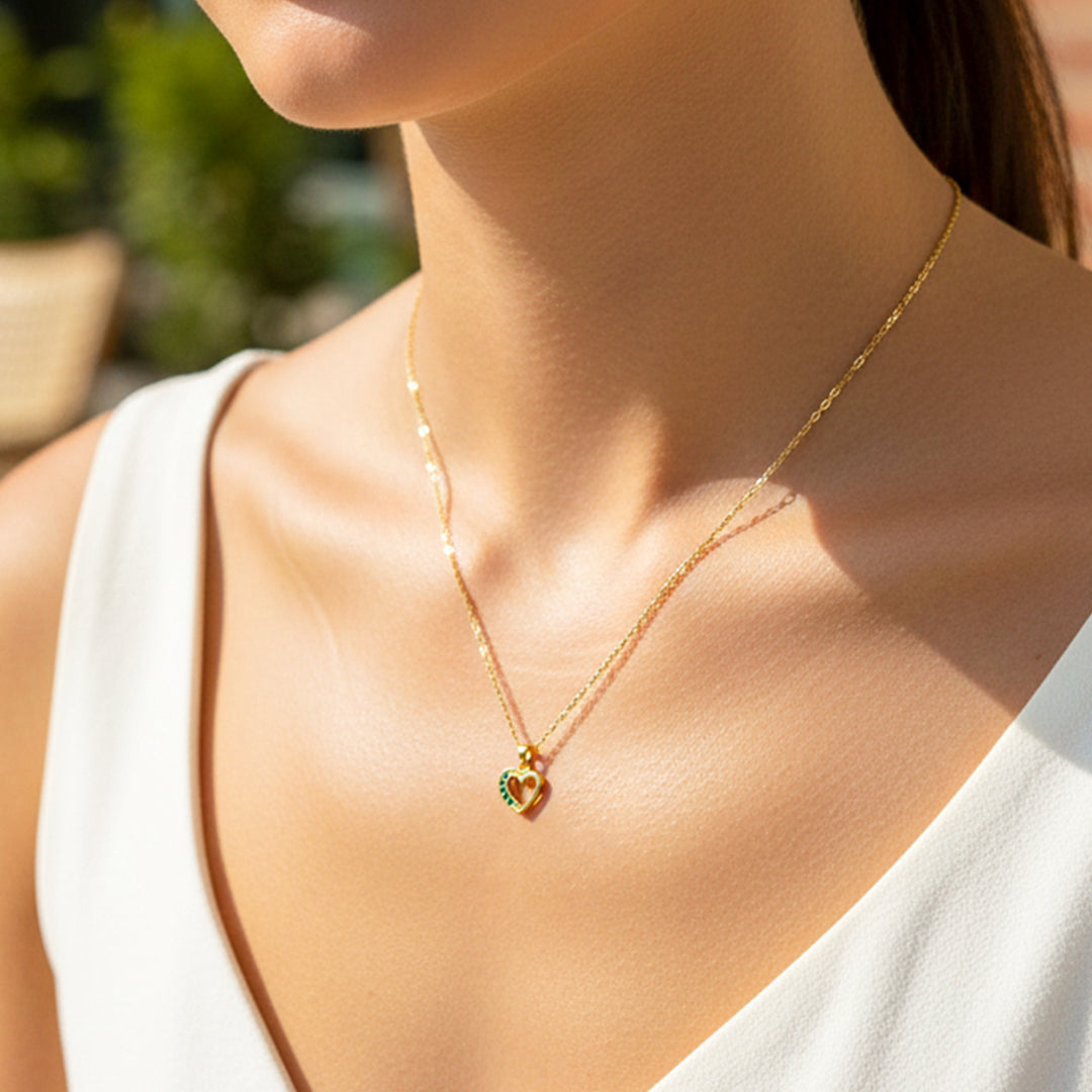 Cuello de modelo usando una cadena con un dije en forma de corazón en oro amarillo de 18 quilates con cristales verdes de Joyería Caracas.