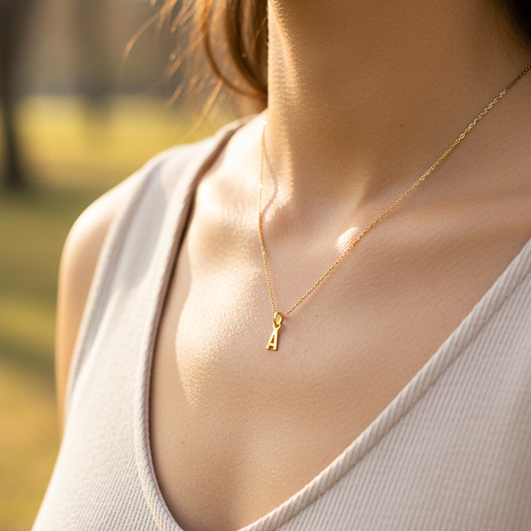 Cuello de modelo usando una cadena con un dije en forma de la letra A en oro amarillo de 18 quilates de Joyería Caracas.