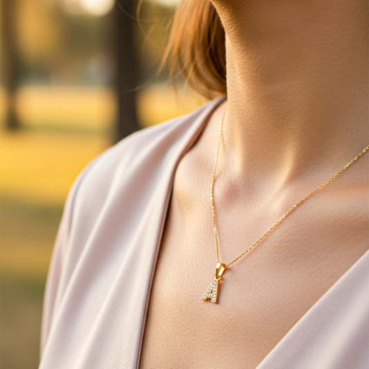 Cuello de modelo usando una cadena con un dije de la letra A en oro amarillo de 18 quilates con cristales de Joyería Caracas.