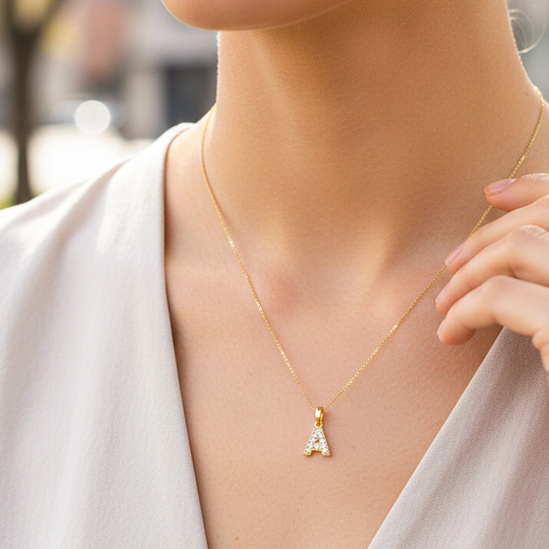Cuello de modelo usando una cadena con un dije en forma de la letra A en oro amarillo de 18 quilates con cristales de Joyería Caracas.
