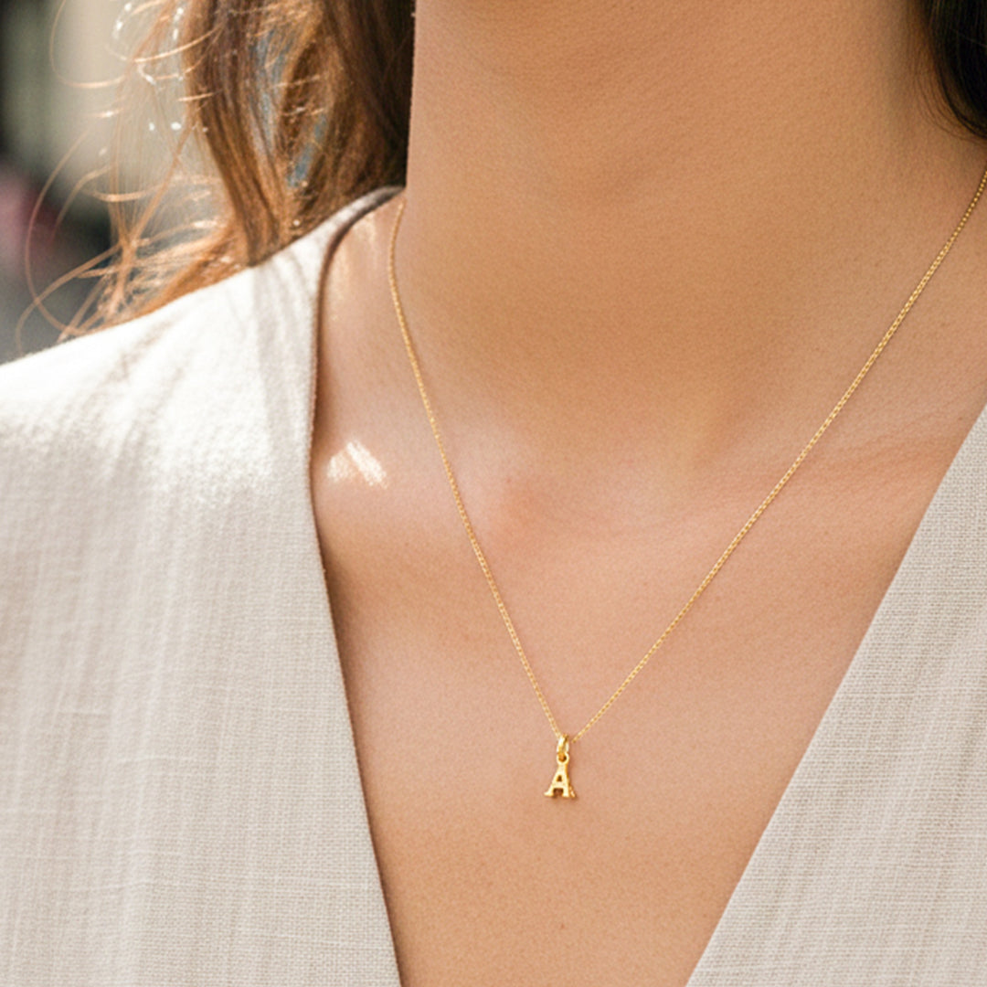 Cuello de modelo usando una cadena con un dije en forma de la letra A mini en oro amarillo de 18 quilates de Joyería Caracas.