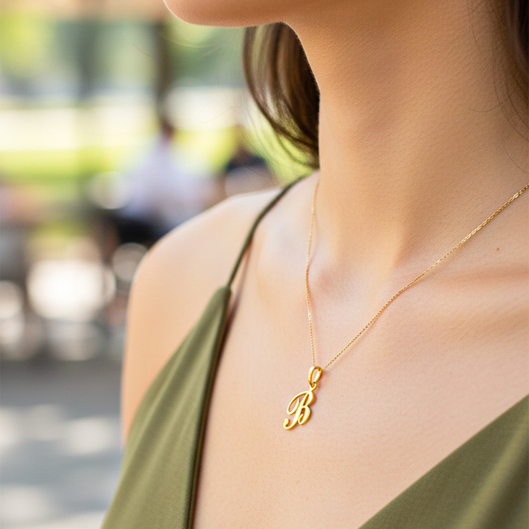 Cuello de modelo usando una cadena con un dije de la letra B cursiva en oro amarillo de 18 quilates de Joyería Caracas.