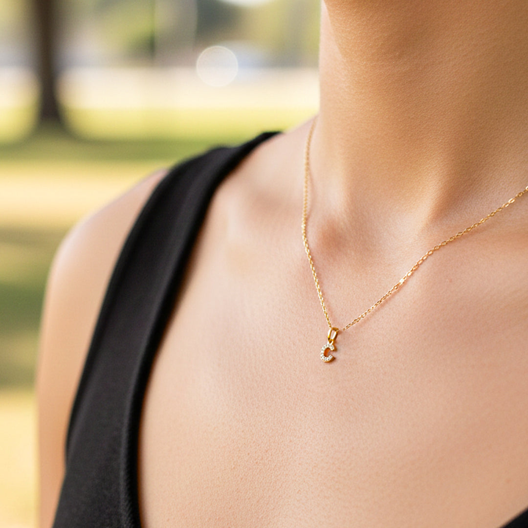 Cuello de modelo usando una cadena con un dije la letra C en oro amarillo de 18 quilates con cristales de Joyería Caracas.