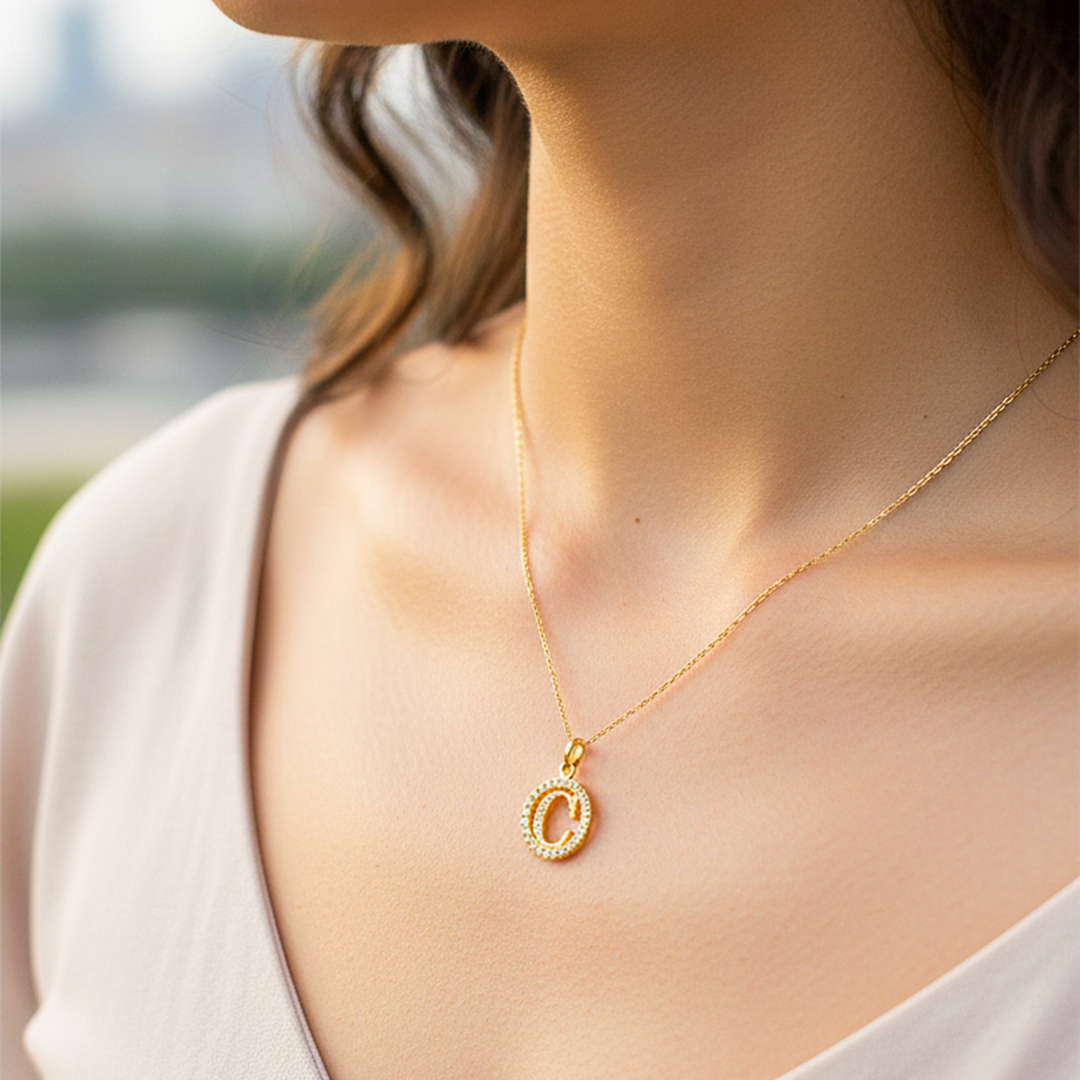 Cuello de modelo usando una cadena con un dije de la letra C en oro amarillo de 18 quilates con cristales de Joyería Caracas.