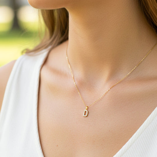 Cuello de modelo usando una cadena con un dije de la letra D en oro amarillo de 18 quilates con cristales de Joyería Caracas.