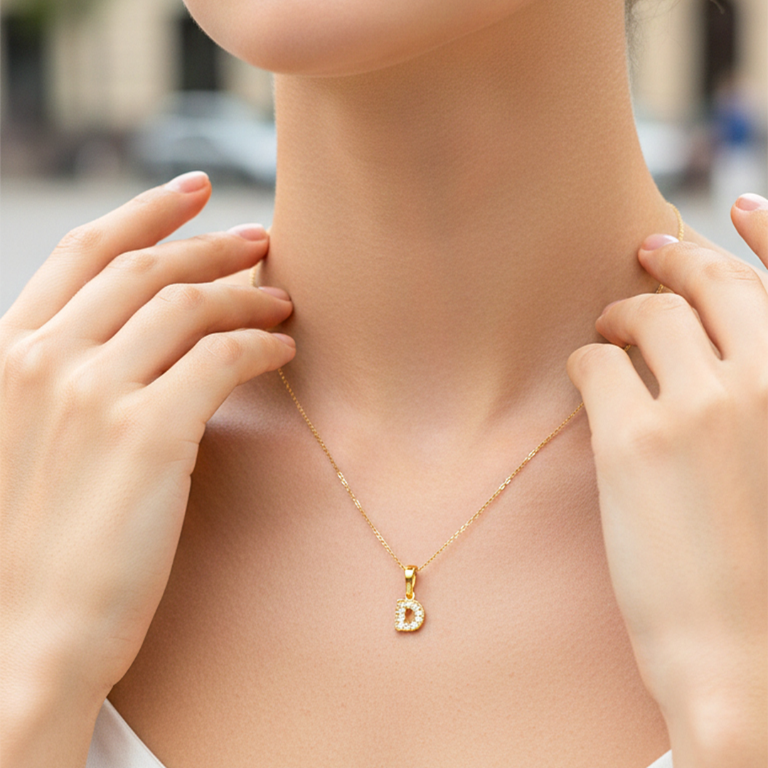 Cuello de modelo usando una cadena con un dije en forma de la letra D en oro amarillo de 18 quilates con cristales de Joyería Caracas.