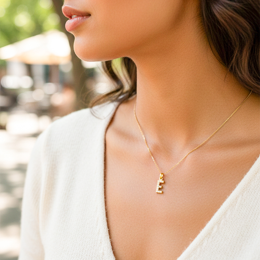 Cuello de modelo usando una cadena con un dije en forma de la letra E en oro amarillo de 18 quilates con cristales de Joyería Caracas.
