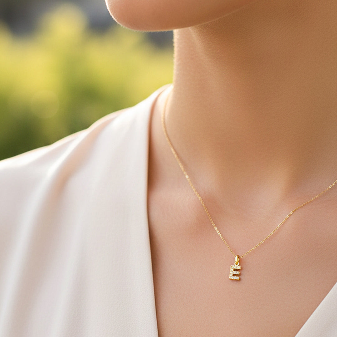 Cuello de modelo usando una cadena con un dije en forma de la letra E en oro amarillo de 18 quilates con cristales de Joyería Caracas.
