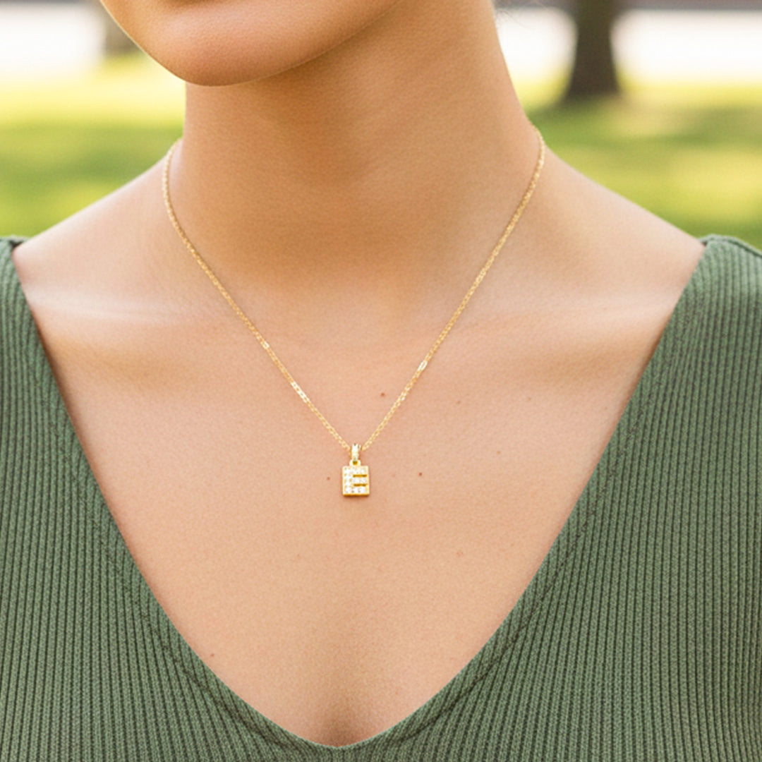 Cuello de modelo usando una cadena con un dije en forma de la letra E en oro amarillo de 18 quilates con cristales de Joyería Caracas.