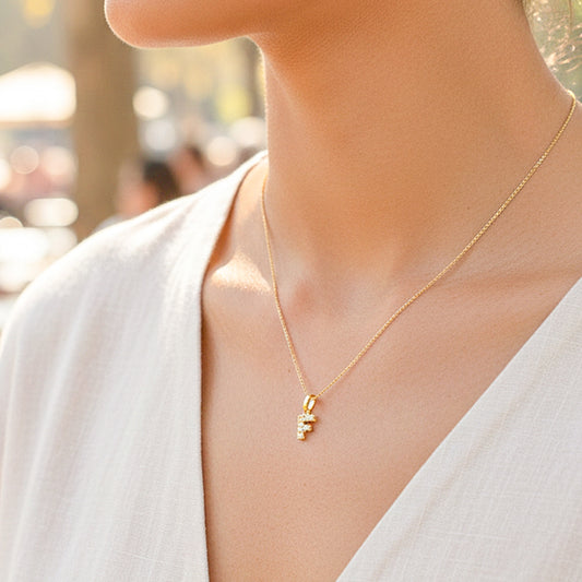 Cuello de modelo usando una cadena con un dije en forma de la letra F en oro amarillo de 18 quilates con cristales de Joyería Caracas.