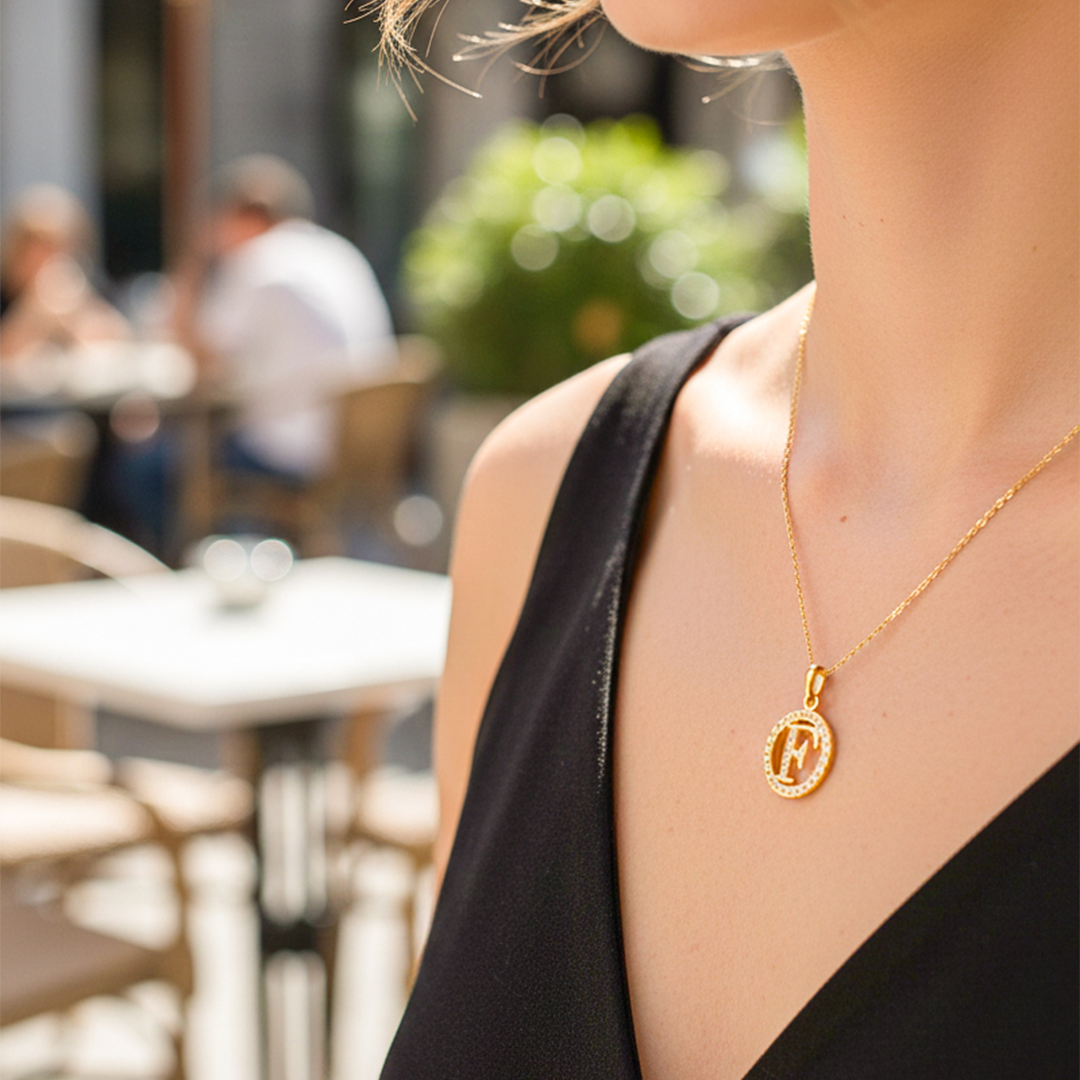 Cuello de modelo usando una cadena con un dije de la letra F en oro amarillo de 18 quilates con cristales de Joyería Caracas. 