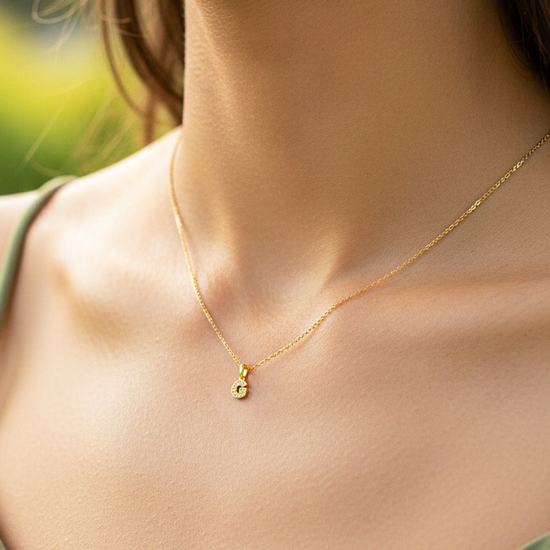 Cuello de modelo usando una cadena con un dije de la letra G en oro amarillo de 18 quilates con cristales de Joyería Caracas.