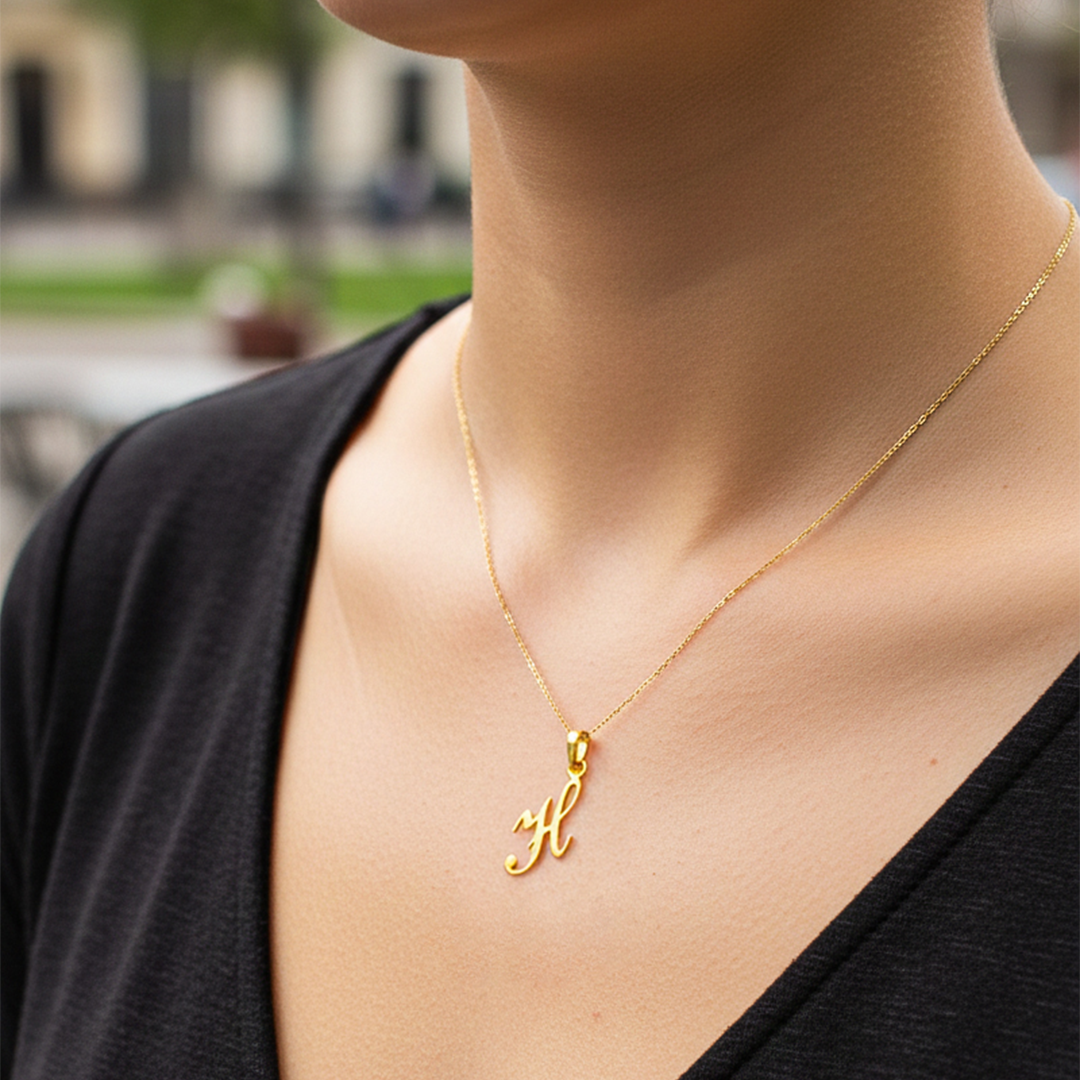 Cuello de modelo usando una cadena con un dije de la letra H cursiva en oro amarillo de 18 quilates de Joyería Caracas.
