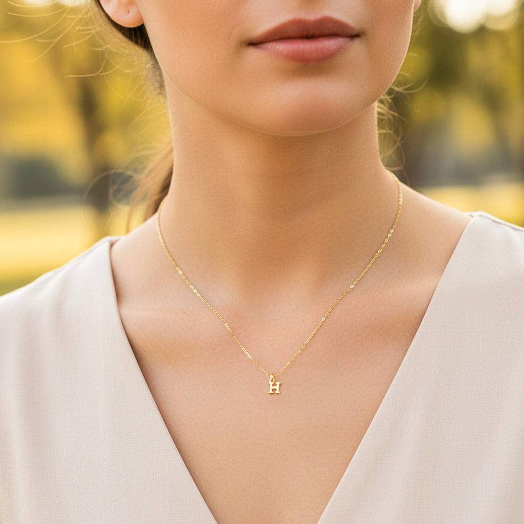 Cuello de modelo usando una cadena con un dije de la letra H mini en oro amarillo de 18 quilates de Joyería Caracas.